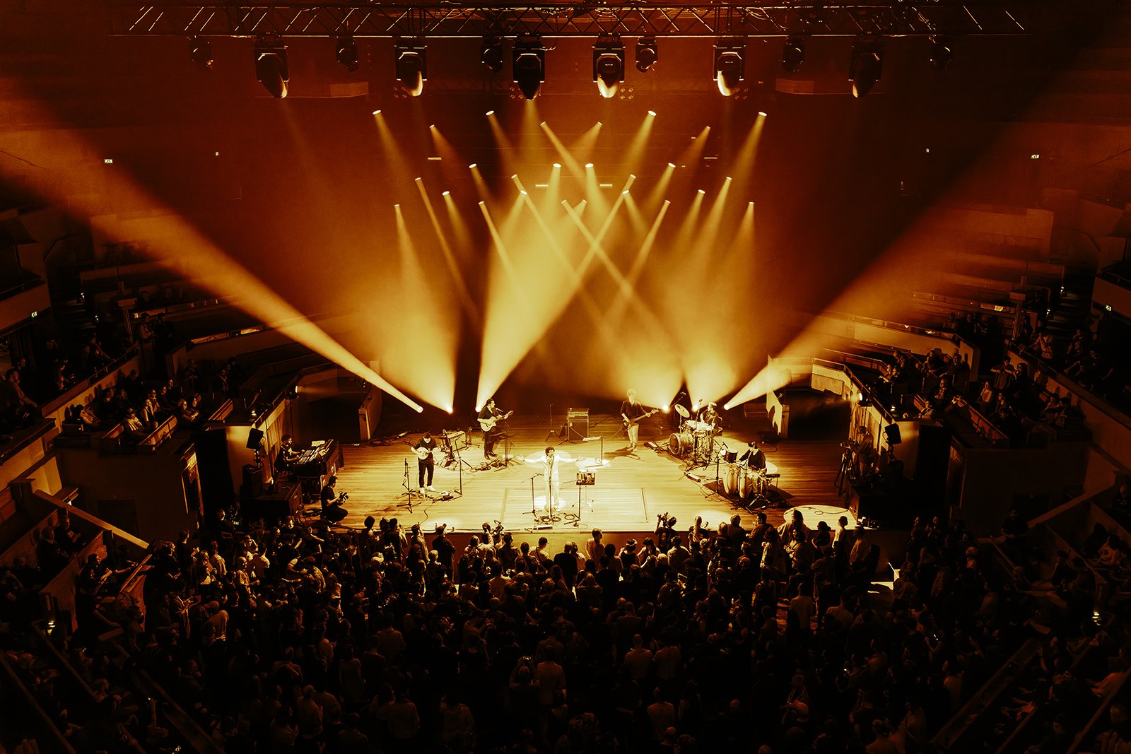 Índio da Cuíca during his performance at Le Guess Who Festival in TivoliVredenburg. Índio da Cuíca and the band are on stage performing, while the audience is standing around them.